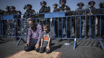 A Palestinian father and son pray under the gaze of Israeli police in East Jerusalem. Photo: Oliver Weiken / EPA