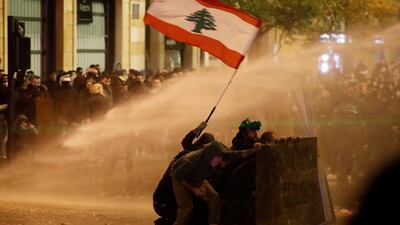 Anti-government protesters wave a Lebanese flag and hide behind a wood barrier from a water cannon as they clash with the riot police during a protest against the new government, near the parliament square, in Beirut, Lebanon, Wednesday, January 22, 2020. AP