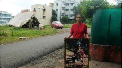 Ayesha Masood, sister of the activist Shehla Masood, with her sibling's picture at the spot where she was shot dead outside her home in Bhopal, India. A policeman stands guard across the road. Gethin Chamberlain for The National
