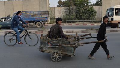 An Afghan child pulls a handcart with a youth sitting on top in Kabul on October 1, 2019. / AFP / Sajjad HUSSAIN