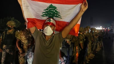 An anti-government protester holds up a Lebanese flag as army soldiers stand guard during a demonstration against deteriorating economic conditions as politicians are deadlocked over forming a new government, in the town of Jal el-Dib, north of Beirut. AP Photo