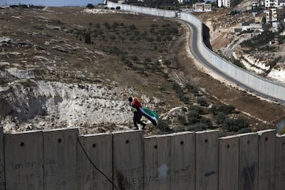 A Palestinian draped in the Palestinian flag walks on top of the Israeli separation wall between the West Bank city of Abu Dis and East Jerusalem, during clashes with Israeli security forces in 2021. AFP