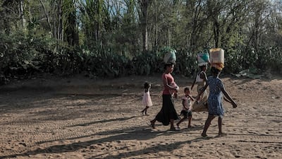 People walk from a market while balancing their purchased food and household supplies on their heads in Ifotaka, in southern Madagascar, on September 23, 2026. The World Meteorological Organization has warned of "increased drought risk" in southern Africa as the El Nino hits in October, with countries across the planet -- from Brazil to India -- also vulnerable. International aid cuts and spiking inflation caused by the Middle East war add to the threat of severe hunger in southern Madagascar. (Photo by Razafindrakoto Mamy Nirina / AFP)