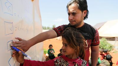A child writes on a fence of a tent as she attends a class conducted by Muheeb al-Essa, 27, a teacher at a camp for internally displaced people in northern Idlib, Syria. Reuters