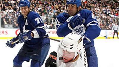 Ryan Carter, in white, of the Ducks, is checked by Jamal Mayers and Pavel Kubina of the Toronto Maple Leafs.