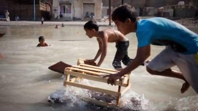 A group of young Kumzari boys cool off by playing and swimming with scrap pieces of wood in a small water hole. Razan Alzayani / The National