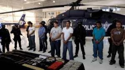 Six alleged members of La Familia are guarded by masked police officers after last week's arrests.