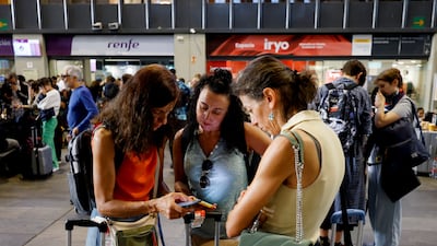 People check their phones for updates at Sevilla Santa Justa station amid delays and cancellations following the collision. Reuters
