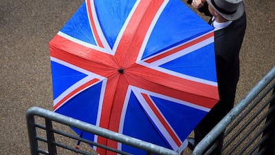 Racegoers shelter from the weather under umbrella. Press Association