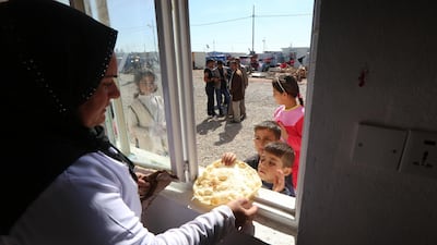 A volunteer from the Emirates Red Crescent distributes bread, made at a bakery run by the non-government organisation, to displaced Iraq children at the Harsham refugee camp. AFP