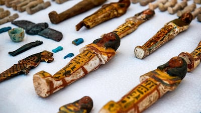 This picture shows carved wooden statues and funerary figurines called Ushabtis made of wood and clay laid out on a table. AFP