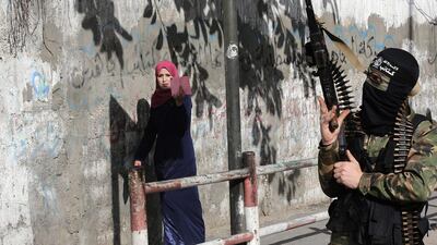 A Palestinian woman uses her phone to film masked gunmen from the Al Mujahideen Brigades, during a rally to mark the 14th anniversary of their movement's foundation, in the east of Gaza City. Mohammed Saber / EPA