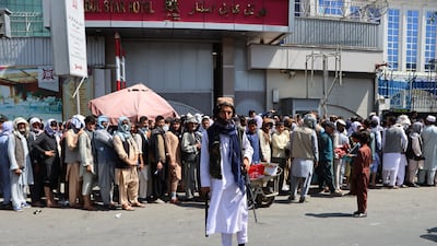 A Taliban fighter stands guard as people line up to withdraw money from banks as limits on withdrawals were set at only 200 US dollars per week, in Kabul, Afghanistan. EPA
