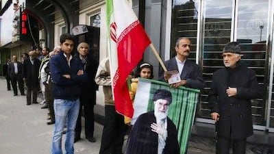 A man holds an Iranian flag and picture of Iran's Supreme Leader Ayatollah Ali Khamenei as he stands in the line to cast his vote during the parliamentary election Friday in Tehran.