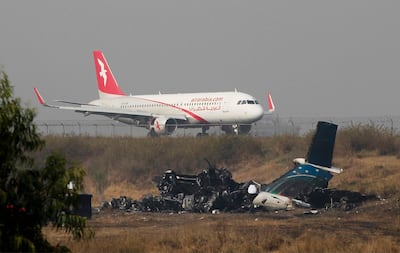 Remains of Bangladesh's US-Bangla Flight BS211 lies on the ground as a plane takes off from Tribhuvan International Airport in Kathmandu, Nepal, Tuesday, March 13, 2018. Niranjan Shrestha / AP Photo.
