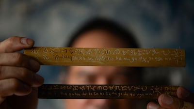 This photo taken on June 11, 2019 shows cultural advocate Leo Emmanuel Castro holding pieces of bamboo inscribed with indigenous Baybayin script at his shop in Manila.