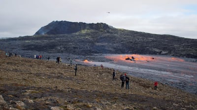 Tourists and other onlookers watch as lava flows from a tunnel near the crater in Geldingadalir valley, southwest of Iceland's capital Reykjavik on September 15, 2021. - Slowly oozing at times, then spurting like a geyser and spitting rocks at others, a volcanic eruption near Reykjavik is still going strong six months after lava began flowing, Iceland's longest eruption since the 1960s. While thousands of curious onlookers have been captivated by the mesmerizing spectacle playing out near Mount Fagradalsfjall since March 19 -- Iceland's sixth eruption in 20 years -- experts say a six-month eruption is not extraordinary. Now officially named Fagradalshraun, or 'beautiful valley of lava' after the nearby Mount Fagradalsfjall, the volcano rose up from a fissure in the ground. It has so far spewed out almost 143 million cubic metres of lava. (Photo by Jeremie RICHARD / AFP)