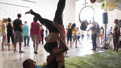 A couple practising Acrobatic Yoga shares a gentle balance while the crowd carries on.