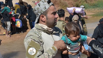 A fighter from the Hashed Al Sahaabi units helps displaced people who fled from battles to oust ISIS from Hawija cross a river in the area of Zarga, about 35km south-east of Kirkuk, on October 4, 2017.