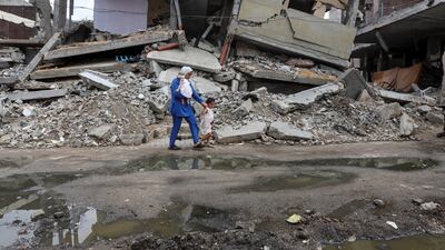 A displaced Palestinian woman walks past the rubble of a house destroyed in an Israeli strike as she returns to her shelter with her daughters in Deir Al Balah. Reuters