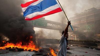 A Red shirt protester carries the Thai flag as tires burn and the violence in central part of the city escalates yesterday.