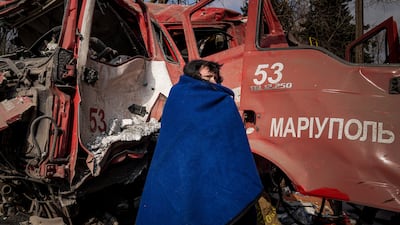 A woman covers herself with a blanket near a damaged fire truck after shelling in Mariupol, Ukraine. AP Photo