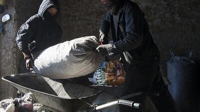 An Afghan youth helps a coal vendor to load a sack of coal onto a wheelbarrow at a shop in Kabul.