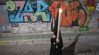 A penitent of the Brotherhood of La Soledad (Solitude) holds a candle as he walks past graffiti while taking part in a Holy Week procession in Almeria, southeast Spain. Holy Week is celebrated in many Christian traditions during the week before Easter. Picture taken April 18, 2014. Francisco Bonilla / Reuters