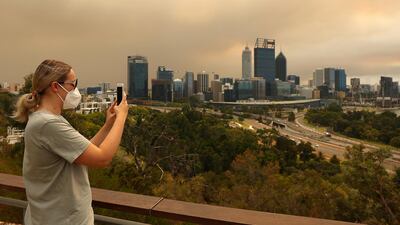 A local resident takes a panoramic image of the bush fire and Perth CBD on her phone from Kings Park. Getty Images