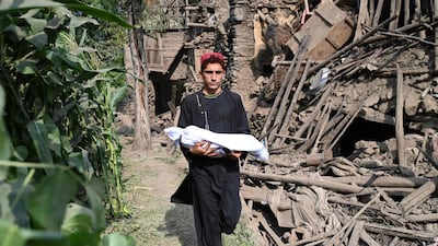 An Afghan carries the body of a relative in a shroud from a ruined house following earthquakes in the Mazar Dara village of Nurgal, eastern Afghanistan. AFP