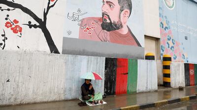 A shoe polisher boy holds an umbrella as he waits for customers under graffiti on a wall in Kabul, Afghanistan April 15. Reuters