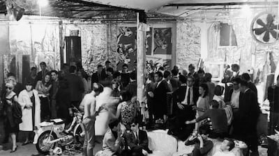 Then: pop artist Andy Warhol's studio The Factory in New York in August 1965. Among those pictured are American photographer Stephen Shore (sitting on couch in foreground, in sunglasses) and filmmaker Shirley Clarke (also on couch, looking through camera). Warhol is also visible at centre rear (at the seam between the cow-print and mylar wallpapers). Fred W McDarrah / Getty Images