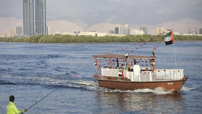 A boat decorated with UAE flags passes a fisherman in RAK. Reem Mohammed / The National