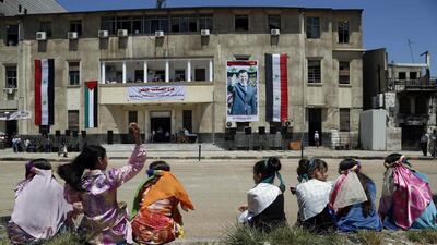 Children sitting on a sidewalk across from a poster of Syrian president Bashar Al Assad hanging on the government telecommunications building in Homs on May 15, 2014. Omar Sanadiki/Reuters