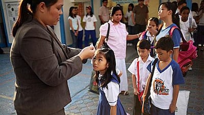 Students at Philippine National School wait their turn yesterday as school nurse Rowena Valera, left, checks the temperature of each child before they enter the classroom.