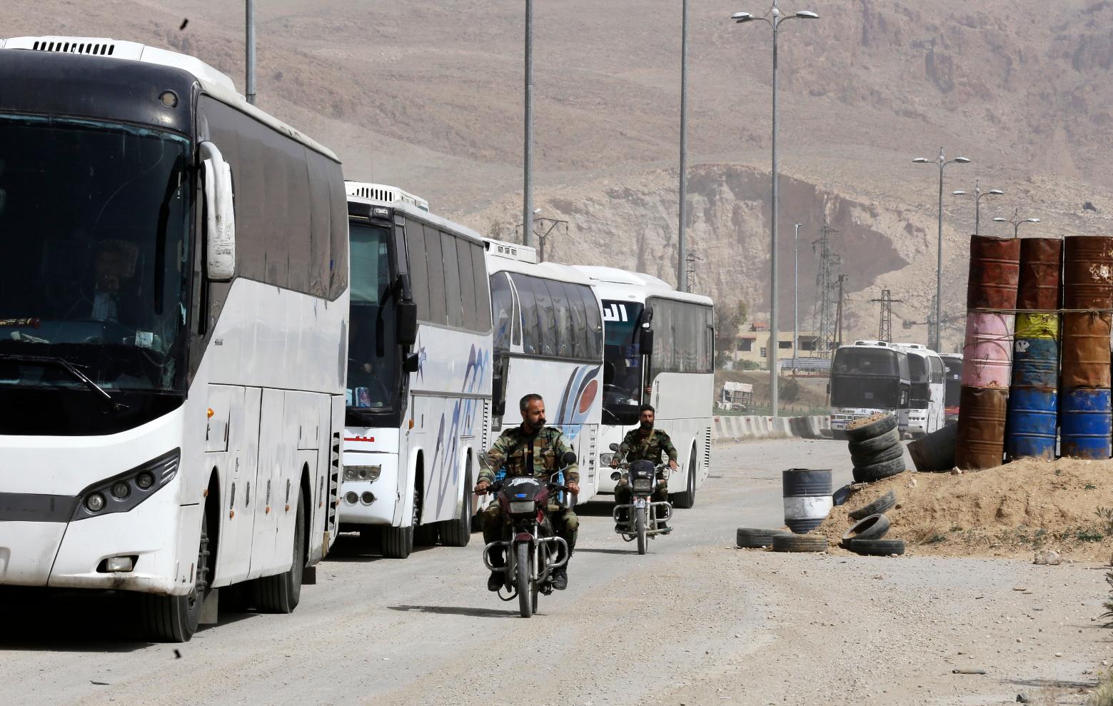 Syrian regime forces drive motorbikes past buses waiting at the entrance of Harasta in Eastern Ghouta, on the outskirts of Damascus, on March 22, 2018. Louai Beshara / AFP