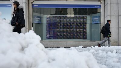 Pedestrians walk past an electronic stock board outside a securities firm as snow covers a sidewalk in Tokyo on Tuesday. Akio Kon / Bloomberg