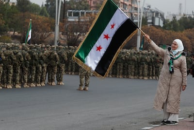 A woman waves the Syrian flag as soldiers stand in formation in Damascus. AP