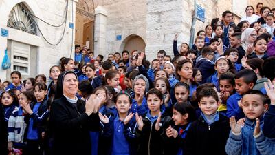 A nun claps along with Palestinian school children as they attend a parade ahead of the arrival of the relic. AFP