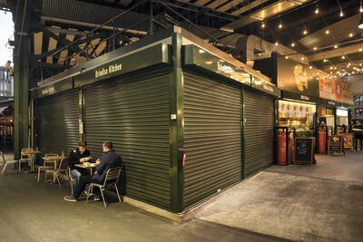 Two men sit at a table outside a closed business in Borough Market, London. Non-essential businesses, including shops and restaurants have been forced to close during lockdowns over the past 12 months. Getty Images