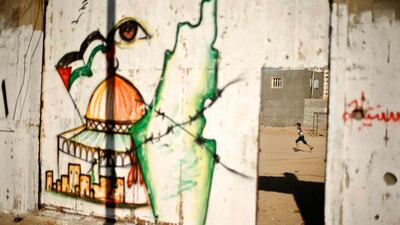 A Palestinian boy plays football as a mural depicts the Dome of the Rock and a map of British Mandate Palestine, on the gate of al-Sadaka club in Gaza City. Mohammed Salem / Reuters