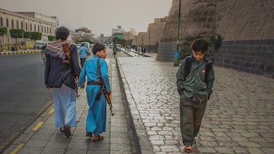 A young boy carrying an AK-47 looks over his shoulder at a boy of a similar age carrying a back-pack, showing the starkly different futures ahead of Sanaa's young generation of children.Ali Alsonidar