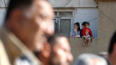 A woman holding her daughter looks at Kurdish and Arab protesters chanting slogans against Turkish President Tayip Erdogan as they walk during a march to the United Nations Headquarters in the town of Qamishli, Syria. REUTERS