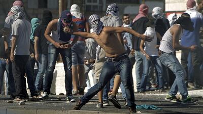 Masked Palestinian protestors throw stones toward Israeli police during clashes in Shuafat neighborhood in Israeli-annexed Arab East Jerusalem, on July 2, 2014, after a Palestinian teenager was kidnapped and killed in an apparent act of revenge for the murder by militants of three Israeli youths. AFP PHOTO / AHMAD GHARABLI