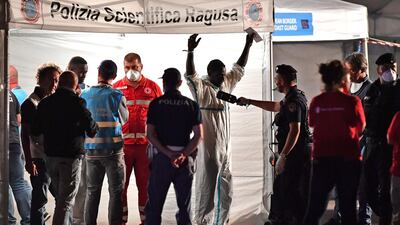 TOPSHOT - A policeman checks a migrant leaving from the Italian Coast Guard vessel Diciotti at the port of Pozzallo, Sicily on June 19, 2018, following a rescue operation of migrants and refugees at sea. / AFP / Giovanni ISOLINO