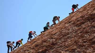Tourists climb the sandstone monolith called Uluru that dominates Australia's arid center at Uluru-Kata Tjuta National Park. AAP Image via AP