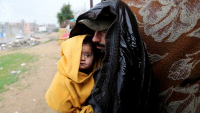 A Palestinian man stands outside with a child on a rainy day in Khan Younis, southern Gaza Strip, on January 16. Reuters