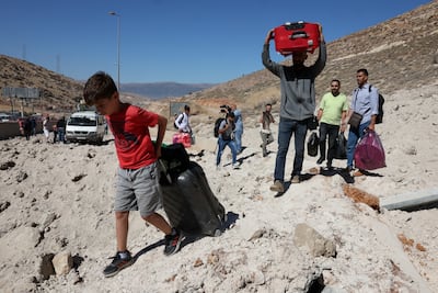 People carry their belongings while walking on the rubble, after an Israeli strike, as they flee Lebanon due to ongoing hostilities between Hezbollah and Israeli forces, at Masnaa border crossing with Syria, in Lebanon, October 4, 2024. REUTERS / Mohamed Azakir