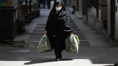 A woman wearing a face mask to protect against the new coronavirus carries her shopping in northern Tehran, Iran. AP Photo