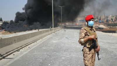 A soldier stands guard as smoke billows from a weapons depot in Idlib province. AFP